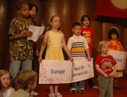 Children gather on stage at the church with signs showing their family's native country or continent.