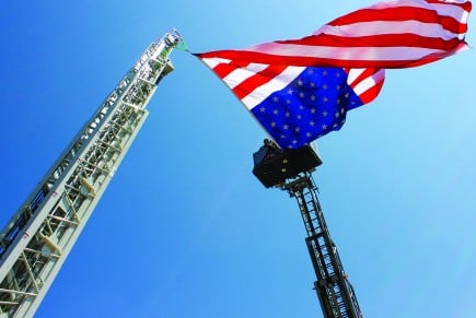 A U.S. flag hangs between two fire truck ladders in West