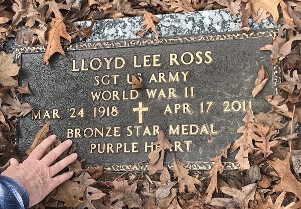 Bob Ross brushes away leaves atop his father Lloyd Ross’ grave marker.