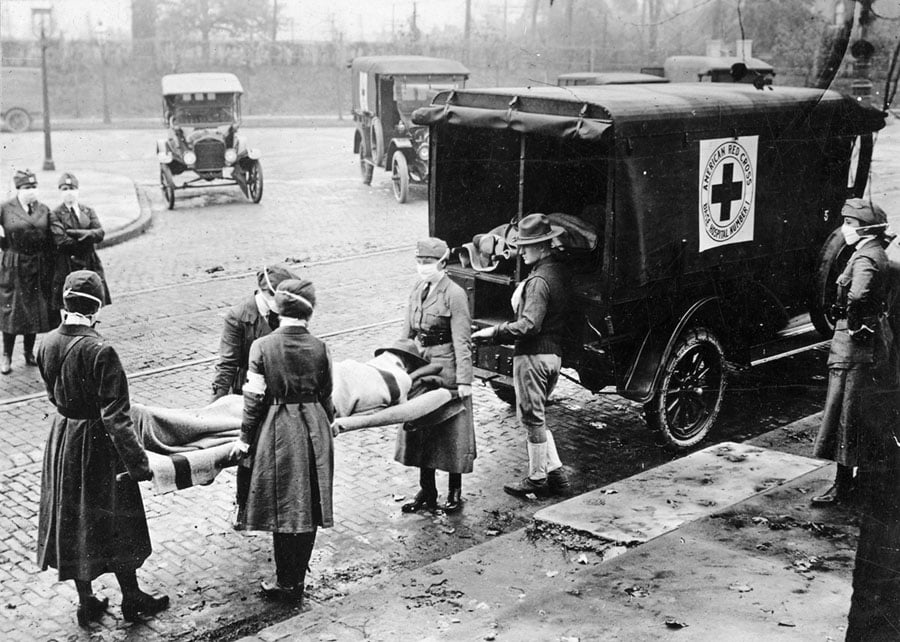 With masks over their faces, members of the American Red Cross remove a victim of the "Spanish flu" from a house in St. Louis in 1918.