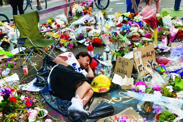 A man rests amid flowers and memorials for George Floyd during protests in Minneapolis. Floyd, 46, was accused of trying to pass a fake $20 bill. He died in police custody.
