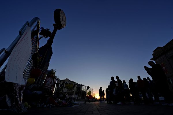 People stand Sunday at a memorial dedicated to the victims of last week's mass shooting in front of Union Station in Kansas City, Mo. Authorities say two juveniles have been charged with crimes connected to the shooting at the Kansas City Chiefs’ Super Bowl rally.