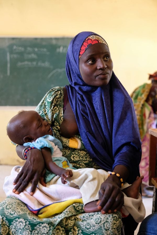 A mother breastfeeds her crying child while a doctor with Hope Springs International discusses the infant's malnutrition diagnoses.