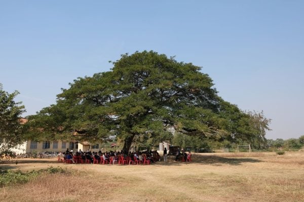 A crowd listens to Sokhom Hun, Mike Meierhofer and Mark Banks preach under a tree.