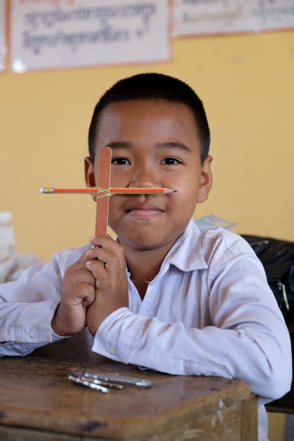 A boy displays a cross — made of a broken rubber band, a pencil and a nail file — during a Bible class hosted by Cambodia Christian Ministries.