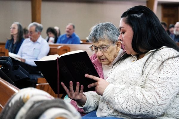 Elizabeth Montemayor holds up a hymnal for Betty Munsell during worship at the Hastings Church of Christ in Nebraska.
