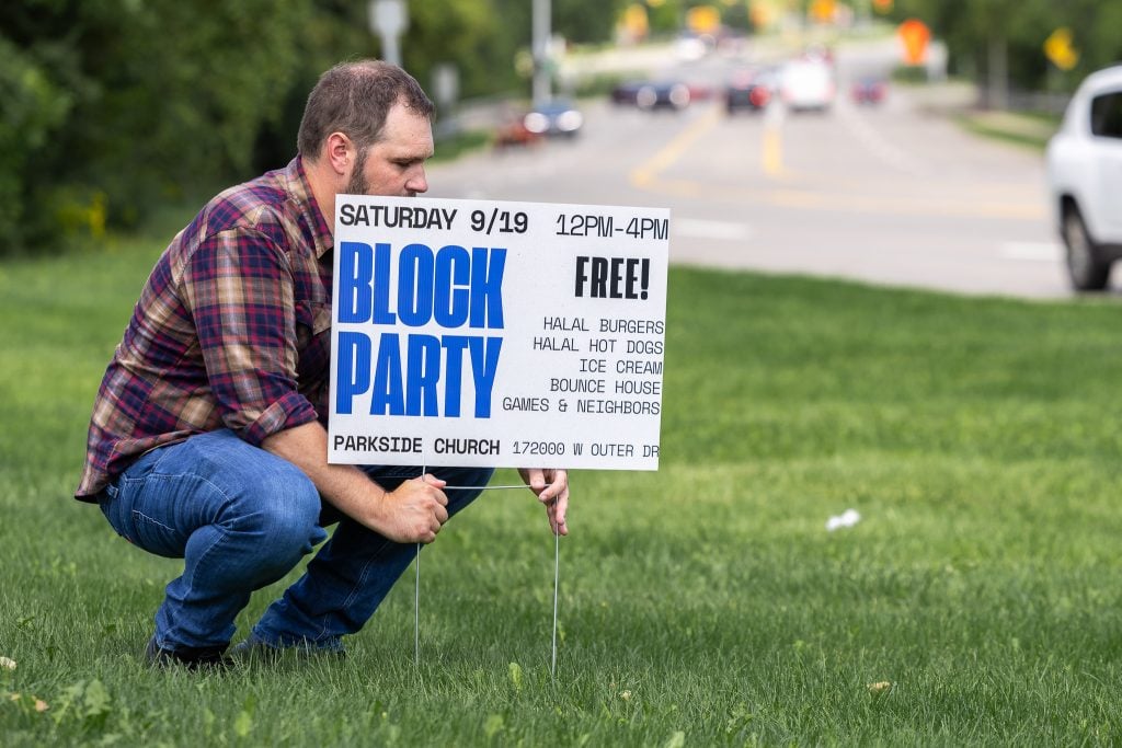 Minister Wayne Beason places a sign by a roadway in Dearborn Heights, Mich., inviting neighbors — including Muslims — to attend a church block party.