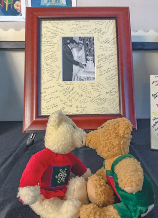 A pair of teddy bears smooches next to a framed photo from Clyde and Gwen Antwine’s wedding in 1956 adorned with inspirational messages from family and friends. 